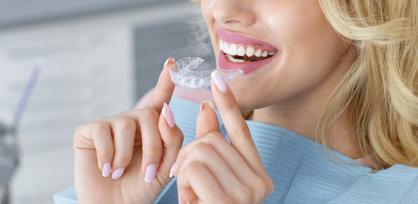 Woman holding a clear dental aligner near her smiling teeth.